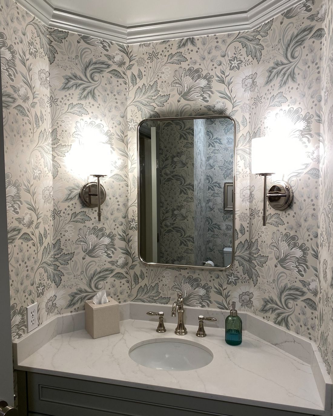 Powder room in blue-grey floral wallpaper with crown molding and marble vanity