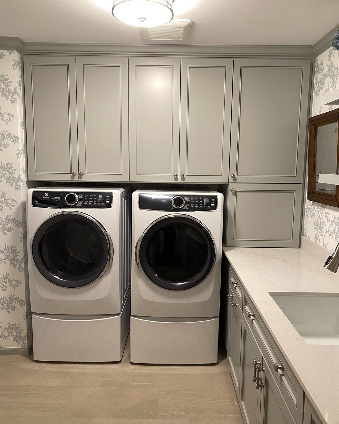 Laundry room with painted cabinets and floral wallpaper