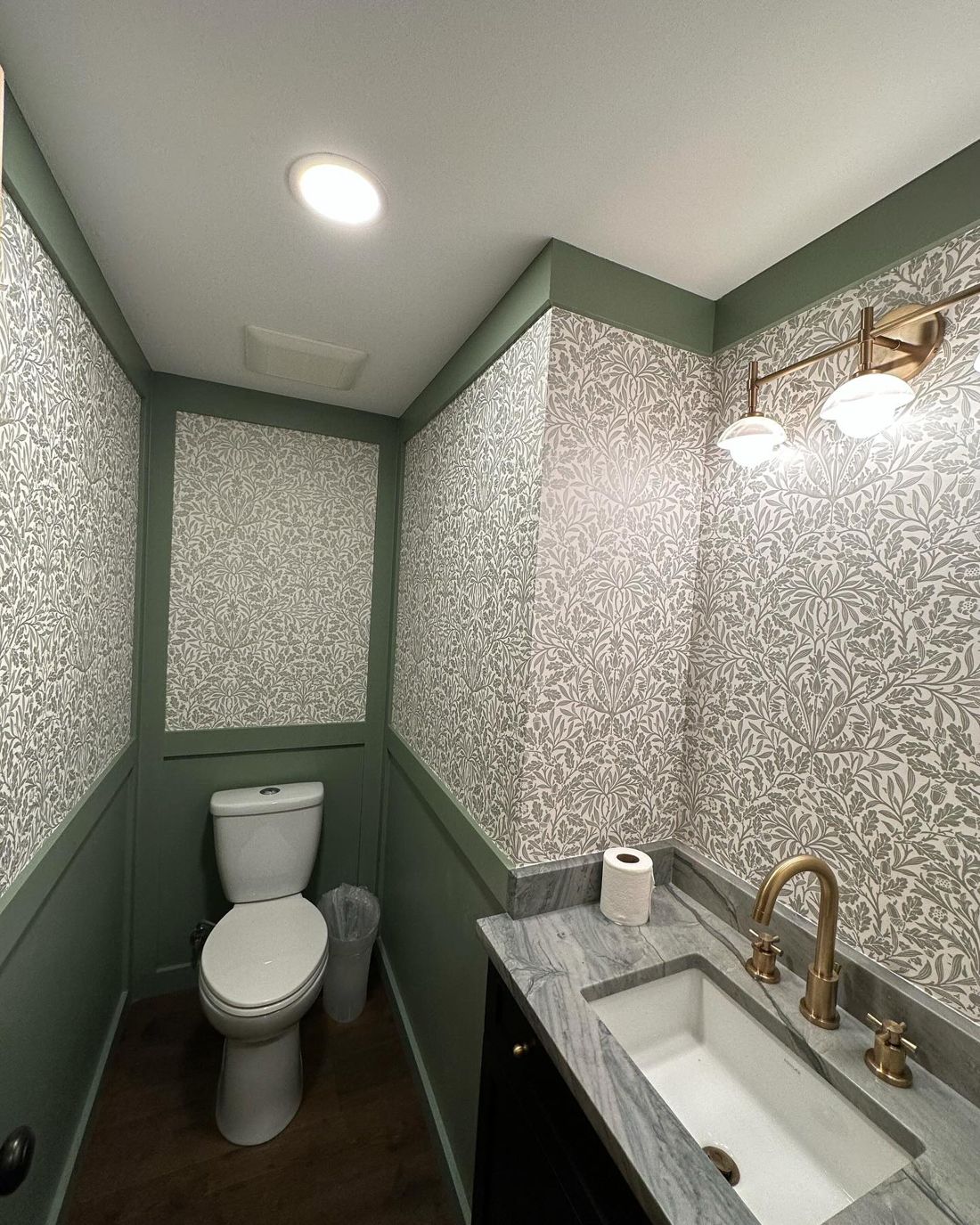 Powder room with green-painted wainscot and leaf wallpaper